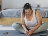 En større ung kvinde sidder på sin yogamåtte og kigger ned på sine samlede fødder.