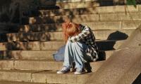 En ung trist pige sidder på et stentrappe, foroverbøjet med hovedet gemt væk.