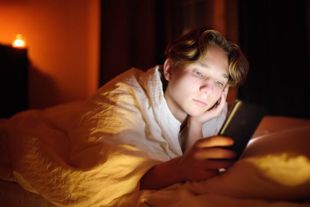 Ung dreng kigger på sin telefon, mens han ligger i sin seng på et værelse