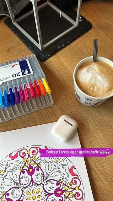Stina der lytter til podcast, tegner og drikker kaffe